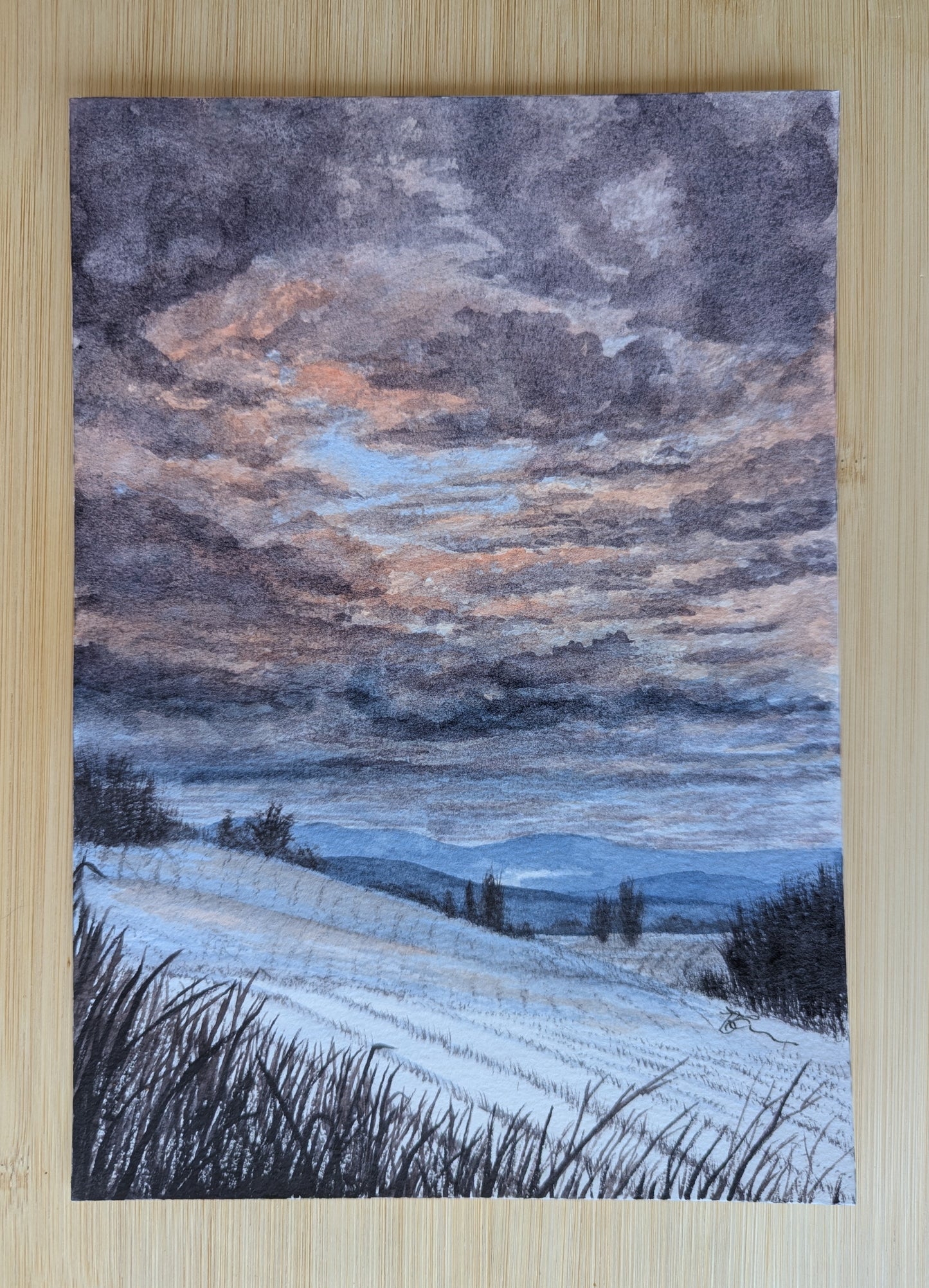 Watercolour painting of a snowy landscape with a dramatic sky on a wooden surface.