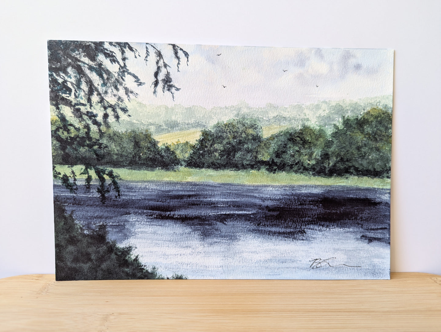 painting of a landscape with a river and trees on a wooden surface.