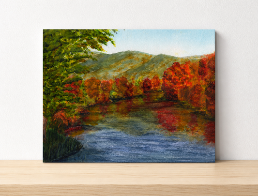 A painting of a lake with vibrant red orange and green trees all the way around the lake and yellow and green mountains in the distance.